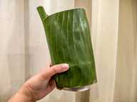 A hand is holding up a banana leaf-wrapped cake mould. A hand is holding up a banana leaf-wrapped cake mould.