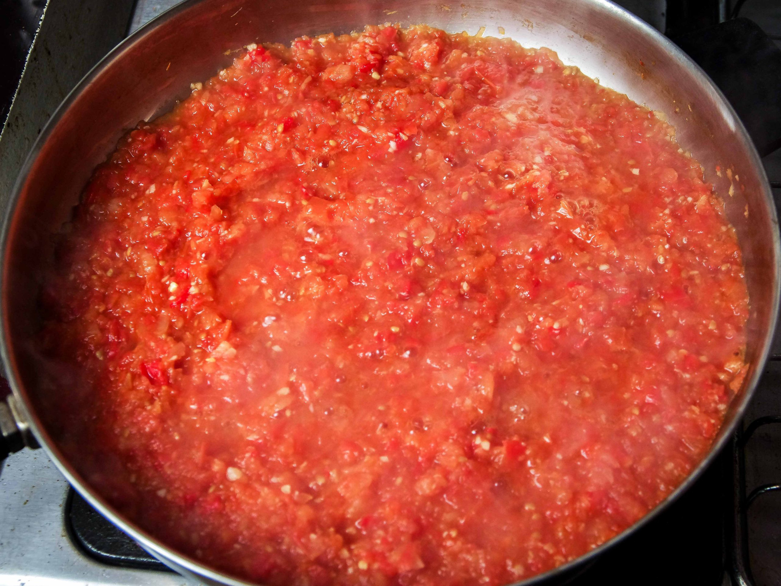 Red tomato sauce reducing in a steel pan.